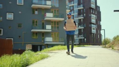 Karton kutu taşıyan çekici bir teslimatçı. Sokak alışveriş paketine yürüyor. Postacı ağır çekimde.