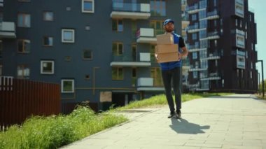 Karton kutuları tutan çekici bir teslimatçı sokak alışveriş paketinin önünde ağır çekimde yürüyor.
