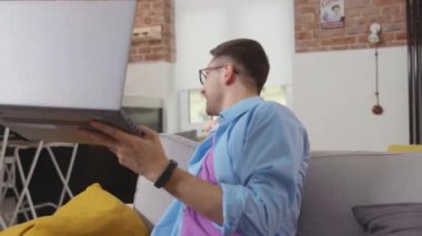 Genç adam kanepede dinlenirken videoyu evde oturup sohbet ederken yetişkin yetişkin yetişkin videosu yavaş çekim profesyonel teknoloji konferansı.