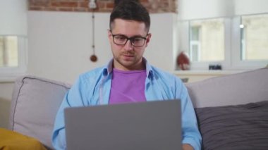 Kanepede oturan yorgun adam bilgisayarını kullanıyor. Evde üzgün, internetten kendini izole eden bilgisayar kullanıyor.