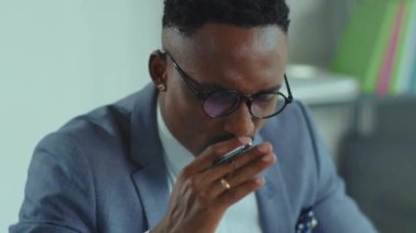 Yüzü yorgun Afrikalı Amerikalı genç adam masasında oturan gözlüğünü çıkardı baş ağrısı projesi iş adamı uzaktan çalışan sosyal ağ teknolojisi yakışıklı dijital internet yavaş çekim