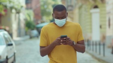 Yüz maskesi takan genç Afro-Amerikalı adam etrafına bak. Sokak koronavirüsüne telefon et. Güvenlik önlemi, salgın salgını, bulaşıcı ve ağır çekim.
