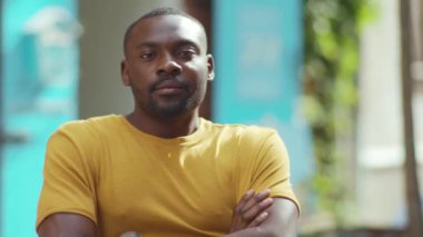 Gülümseyen Afrikalı Amerikalı adam, sokak şehrindeki kamera standına bak. Neşeli siyah portre, güneşli, kentli, yakışıklı, kendine güvenen, yavaş çekim.