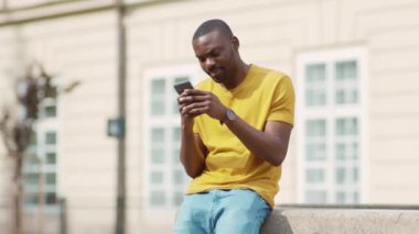 Yakışıklı, Afro-Amerikan, çekici bir adam telefon kulübesi kullanıyor, gülümsüyor, günbatımı, cep telefonu moda interneti, teknolojinin dışında, yavaş çekim.