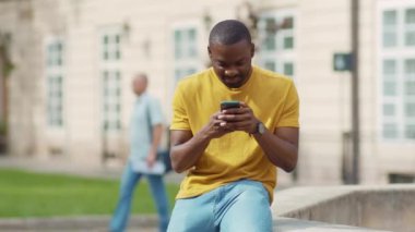Çekici Afro-Amerikalı genç çekici adam telefon kulübesini kullanıyor gülümsüyor gün batımı cep telefonu moda interneti teknolojinin dışında yavaş çekim