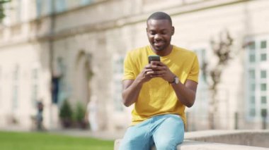 Genç Afrikalı Amerikalı çekici bir adam telefon kulübesinde gülümsüyor güneş ışığı günbatımı cep telefonu moda interneti teknolojinin dışında yavaş çekim