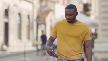 Mutlu Afro-Amerikan çekici bir adam sokakta yürürken gülümsüyor güneş ışığı günbatımı cep telefonu moda interneti teknolojinin dışında yavaş çekim