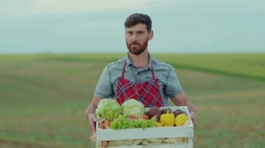 Çiftçi genç adam elinde organik sebzelerle gülümseyen kameraya bak. Tarım tarlası, tarım, tarım, tarım, bahçe, organik, açık hava. Yavaş çekim yakın çekim.