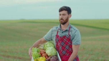 Yakışıklı çiftçi, elinde organik sebze dolu bir kutuyla kameraya bak. Tarım, tarım, tarım, tarım, bahçe, organik, açık hava, yavaş çekim yakın çekim.