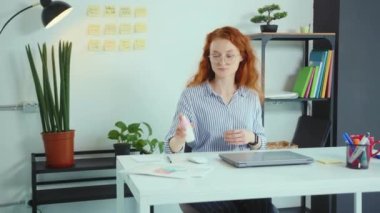 Çekici genç bir kadın dizüstü bilgisayarı kullanmadan önce sprey sıkarak ellerini ovuyor ofis Corona virüs koruma kavramını yavaş çekimde kullanıyor.