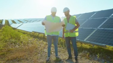 Güneş çiftliğinde özel üniformalı iki mühendis güneşli pillerin montajını tartışıyor. Elektrik yavaş çekim.