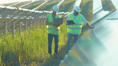 Mühendisler güneş çiftliğinde dizüstü bilgisayar ve proje planı kullanıyorlar. Etrafa bakınıp güneşli pillerin kurulumunu tartışıyorlar. Elektrik yavaş çekim.