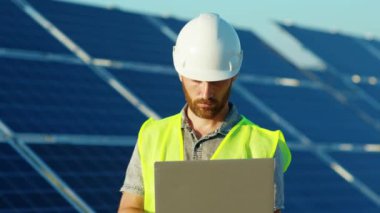 Çekici mühendis dizüstü bilgisayar kullanıyor. Güneş pillerinin yakınındaki kameraya bakın. Yenilenebilir enerji işçisi teknolojisi.