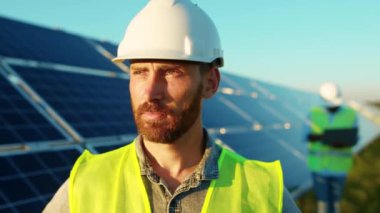 Yüz genç adam, güneş pillerinin yakınındaki kameraya bak güneş ışığı teknolojisinde yenilenebilir enerji işçisi modern elektrik enerjisi yavaş çekim