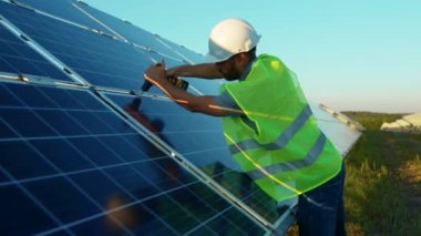Yavaş çekim işçisi güneş panelini güneşli bir günde yeşil bir çatı mühendisi fotovoltaik elektrik bataryasıyla metal bazlı matkapla tamir ediyor.