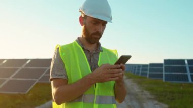 Portre genç adam güneş pillerinin yanında telefon standı kullanıyor güneş ışığı teknolojisinde yenilenebilir enerji işçisi modern elektrik enerjisi yavaş çekim