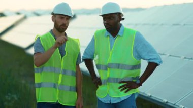 Afrika kökenli Amerikalı ve Kafkas mühendisleri güneş çiftliğinde özel üniformalarla dikilip güneşli pillerin montajını tartışıyorlar. Elektrik yavaş çekim.