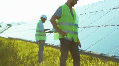 İki işçi güneş panelini metal bazlı matkapla tamir ediyor ve güneşli bir günde yeşil bir çevresel çatı mühendisi fotovoltaik elektrik yavaş çekimde bilgisayarla kontrol ediyor.