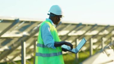 Çalışan Afrikalı Amerikalı adam güneş pillerinin yanında dizüstü bilgisayar standı güneş ışığı teknolojisinde yenilenebilir enerji işçisi modern elektrik yavaş çekim
