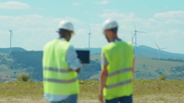 İki mühendis, tarlalarda yel değirmenlerinin yanında dizüstü bilgisayar standı kullanıyor. Ekip, iş birliği, rüzgar enerjisi, tarım teknisyenleri yavaş çekim konuşuyorlar.