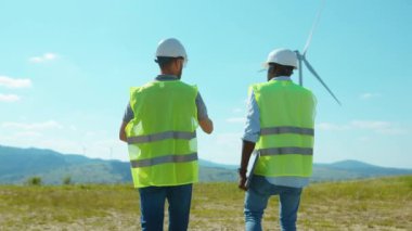 Üniformalı mühendisler tarlalardaki yel değirmenlerinin yanında tartışırken ekip işgücü işbirliği rüzgar enerjisi tarım teknisyenleri yavaş çekim konuşuyorlar.