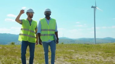 Yürüyen iki ciddi mühendis, tarlalarda yel değirmenlerinin yanında tartışıyorlar. İş birliği, rüzgar enerjisi, tarım teknisyenleri yavaş çekim konuşuyorlar.
