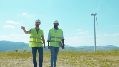 Yürüyen iki mühendis tarlalardaki yel değirmenlerinin yanında tartışıyorlar iş birliği rüzgar enerjisi tarım teknisyenleri yavaş çekim konuşuyor.