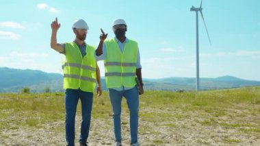Yürüyen iki mühendis tarlalardaki yel değirmenlerinin yanında tartışıyorlar ekip işgücü işbirliği rüzgar enerjisi tarım teknisyenleri yavaş çekim konuşuyorlar.