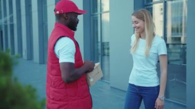 Afrika kökenli Amerikalı teslimatçı kadın müşteriyi cep telefonuyla ödeme üniforması için ödeme yaparken çekmişler. Dışarısı ağır çekim kapalıymış.