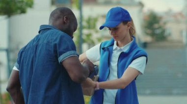 Mavi şapkalı genç kadın kurye, Afrika kökenli Amerikalı müşteriler için cep telefonuyla ödeme üniforması nakliyesi için ödeme yapıyor.