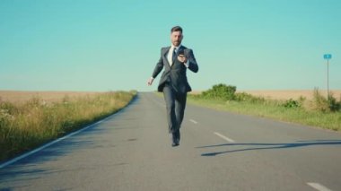 Yavaş çekim işadamı, buğday tarlası özgürlük kavramının yakınındaki akıllı telefon kır yolunda koşuyor.