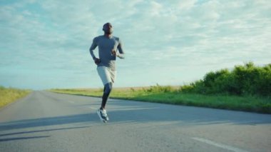 Atletik Afrikalı Amerikalı bir adam güneşli yol maratonunda koşuyor sağlıklı aktiviteler yapıyor genç açık havada ağır çekim egzersiz yapıyor.