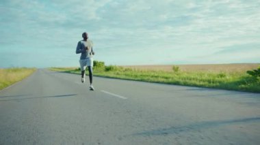 Kapalı kapılar ardında Afro-Amerikalı bir adam güneşli yol maratonunda koşuyor sağlıklı spor yapıyor genç açık havada ağır çekimde egzersiz yapıyor.