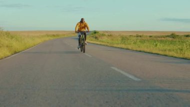 Güzel bir manzarada gülümseyen Afrikalı Amerikalı yolda bisiklet süren mutlu bisiklet bisikleti süren aktif bisiklet bisikleti olan rahatla, gün ışığını yavaş çekimde sür.