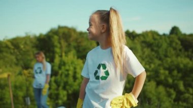 Çevreye gülümseyen küçük bir kızın portresi kameraya gülümsemesine arka planda beyaz bir tişört giyip geri dönüşümlü aile ekolojisi ekolojik toplum eldivenleri yavaş çekim