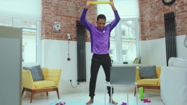 Afrikalı Amerikalı bir adam online antrenörle egzersiz yapıyor. Evde dizüstü bilgisayar kullanıyor. Spor salonunda spor amaçlı lastik bantlar kullanıyor.
