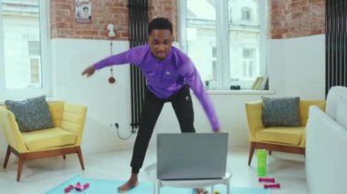 Yavaş hareket eden Afrikalı Amerikalı adam spor giyim sporu aktivitesi için spor salonunda dizüstü bilgisayar kullanarak online antrenörle egzersiz yapıyor.