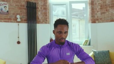 Evde Afrikalı Amerikalı bir adam spor kıyafetleri spor antrenmanında spor eğitimi alan hafif çekimde dizüstü bilgisayar kullanarak online antrenörle egzersiz yapıyor.