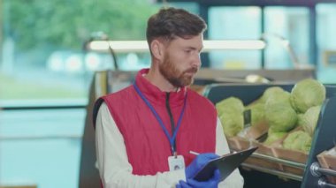 Ciddi genç satıcı, süpermarkette çek yazar. Sebze işi. Güzel, taze, perakende satış mağazası.