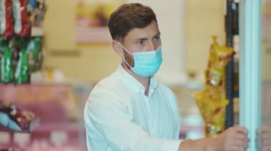 Maskeli adam süpermarkette duruyor. Kameraya bak. Müşteri kiti, dükkan, market, market, perakende, yavaş çekim.