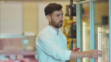 Süpermarkette maske takan çekici bir adam, müşterinin alışveriş listesine bakıyor. Müşteri işyeri, yiyecek dükkanı, market, erkek perakende, yavaş çekim.