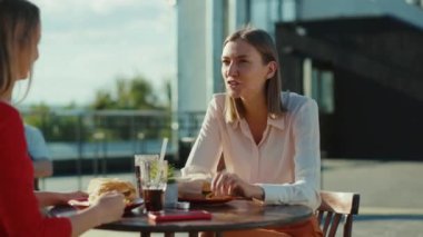 İki neşeli kadın dinlenip kokteyl içerek konuşuyor. Kafe caddesinde burger yiyorlar. Kafeteryada arkadaşça modeller yapıyorlar.