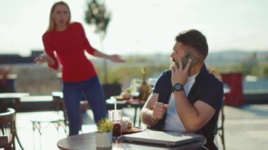 Genç, mutlu, yakışıklı bir adam kafede oturmuş telefonda konuşuyor. Arka planda patates kızartması yiyor. Kadın onunla tartışıyor.