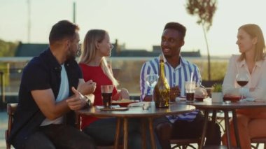 Genç mutlu arkadaşlar sokak kafeteryasında buluşup kokteyl içerek gülümsüyor hafta sonu şehir partileri tatil arkadaşlığı şenlikleri yavaş çekimde konuşuyorlar.