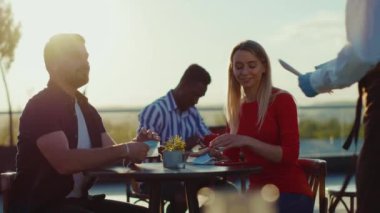 Parktaki masada oturan mutlu genç çift yemek siparişi veriyor garsonluk yapıyor hafta sonları yemek satan adam kafenin önünde perakende satış siparişi satıyor.