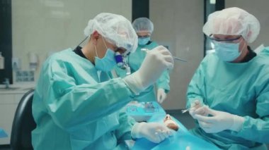 NEW YORK - 5 Nisan 2020: Kapalı diş hekimi koruyucu giysisi ve eldiven giyin ve hasta diş cerrahisinde yardımcı ekip çalışması tıbbi hastalık hijyeninin yavaş ilerlemesine yardımcı olun