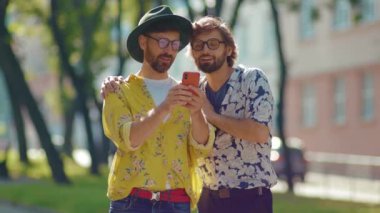 Sevimli iki eşcinsel gün ışığında telefon eder mutlu homoseksüel çift LGBT ile çıkar açık havada gülümsemeyi sever erkek arkadaş ağır çekimde çekicidir.