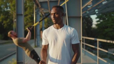 Gülümseyen Afrikalı Amerikalı adam, trx fitness halatıyla hareket ettikten sonra kameraya bakıyor. Stadyum kaslı spor kıyafetleri spor salonunda vücut egzersizleri yapıyor. Yavaş çekimde spor portresi kapanıyor.