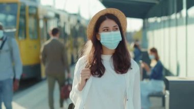 Tıbbi maskeli güzel bir kadının portresi otobüs durağına bakıyor. Pozitif ruh hali turistleri yaz tatillerinde dinleniyorlar. Salgın karantina yavaş çekim.