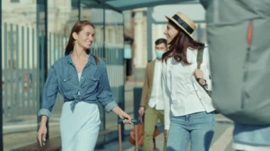 Mutlu iki genç kadın otobüs durağında yürürken konuşan kadın turistler tren istasyonu gezginleri Coronavirus sosyal mesafe salgını ağır çekim